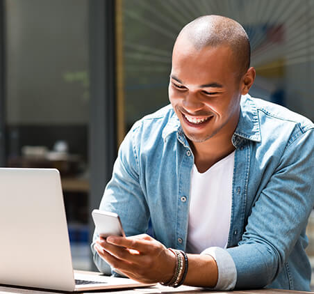 smiling man looking at phone while on computer