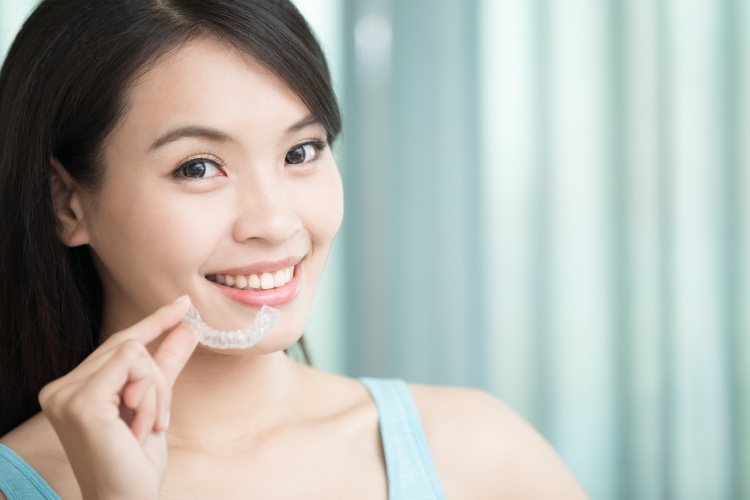 Smiling brunette girl holding her Invisalign clear aligner near her face