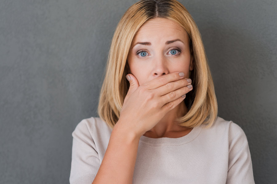 Blonde woman covers her mouth due to fear of halitosis or bad breath.