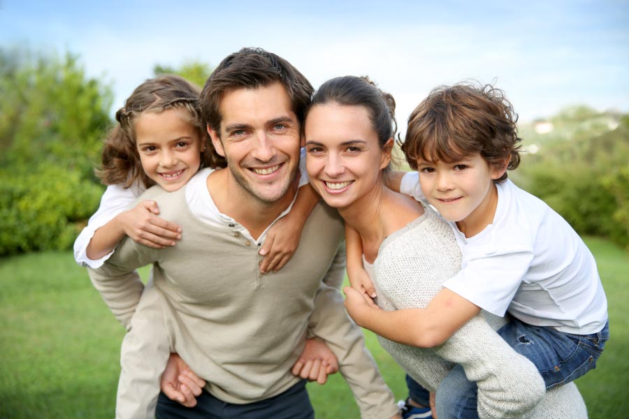 Smiling young family with a little girl and boy on the backs of the mom and dad.