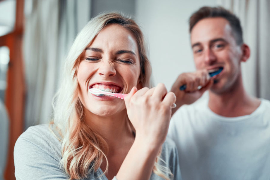 Couple brushing their teeth in front of mirror.